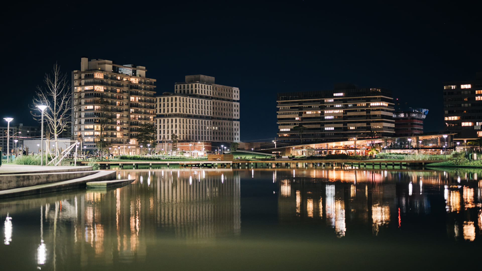 Edifícios iluminados refletidos no lago do Parque Una Pelotas durante a noite